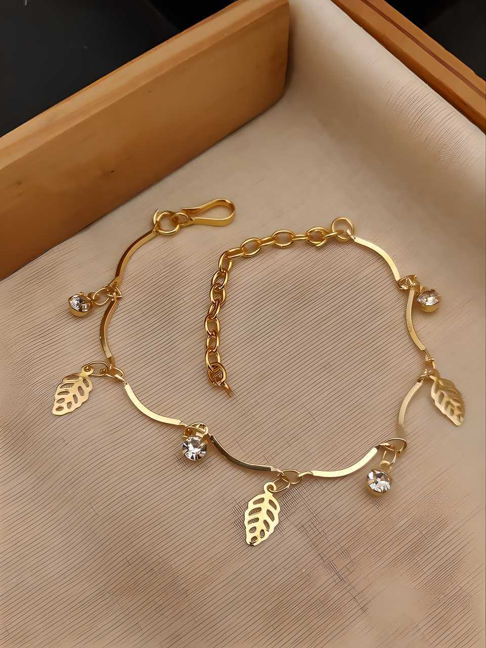 Gold bracelet with leaf charms on a beige surface
