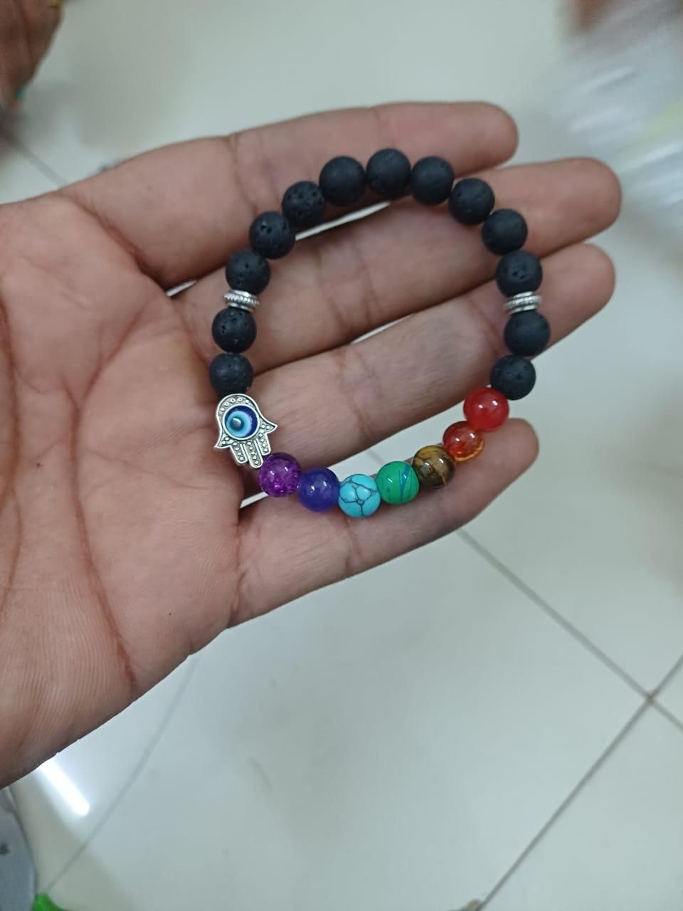 A multicolored beaded bracelet with a black lava stone base and a silver-colored hamsa hand charm
