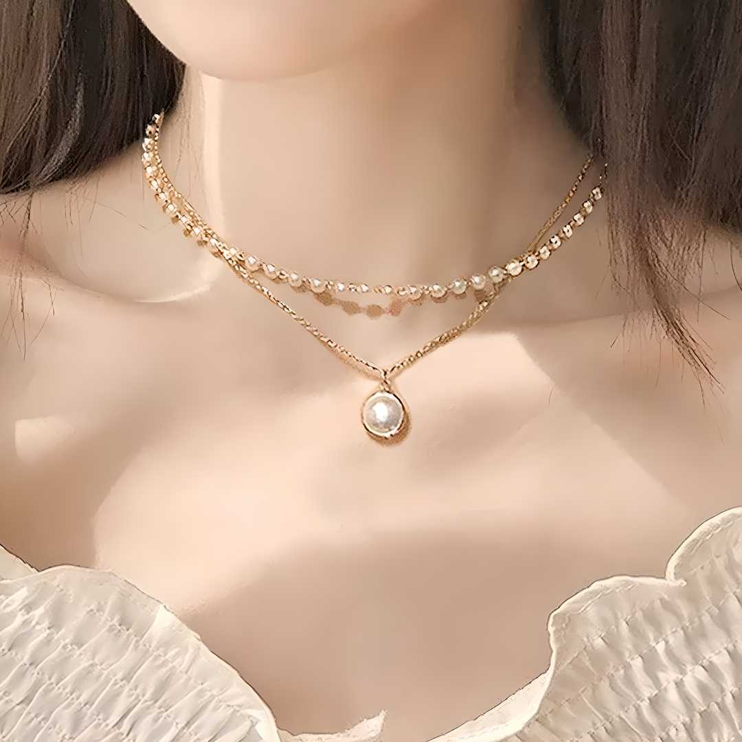 A woman wearing a gold-plated chain necklace with a pearl pendant, layered with a shorter, beaded chain necklace.