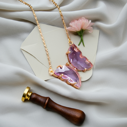 A gold-plated necklace with a stylish butterfly pendant, featuring multicolor (purple and pink) accents on a chain, displayed against a pink fabric background.
