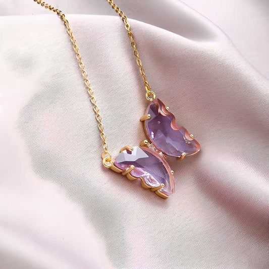 A gold-plated necklace with a stylish butterfly pendant, featuring multicolor (purple and pink) accents on a chain, displayed against a pink fabric background.