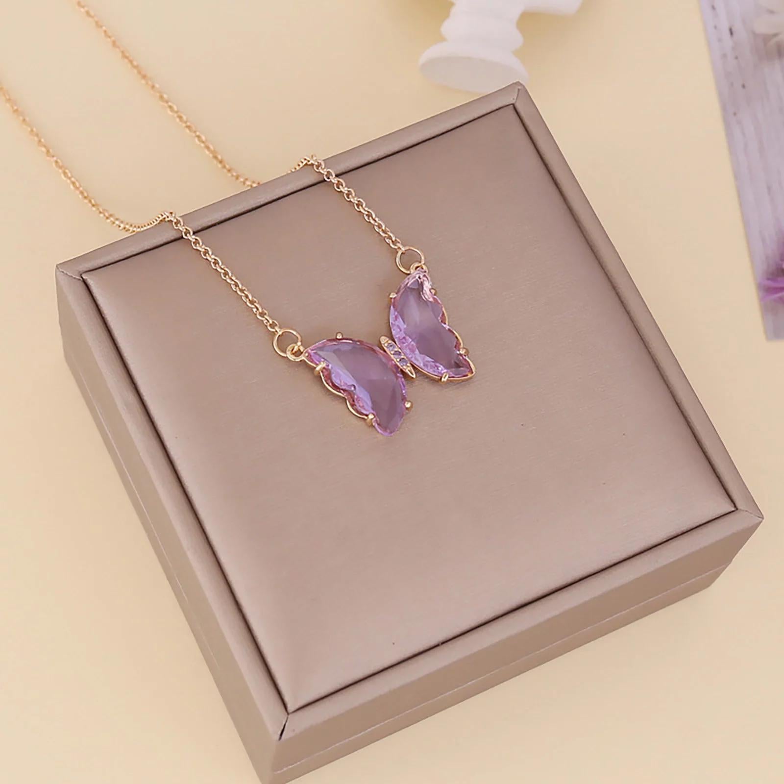 A gold-plated necklace with a stylish butterfly pendant, featuring multicolor (purple and pink) accents on a chain, displayed against a pink fabric background.