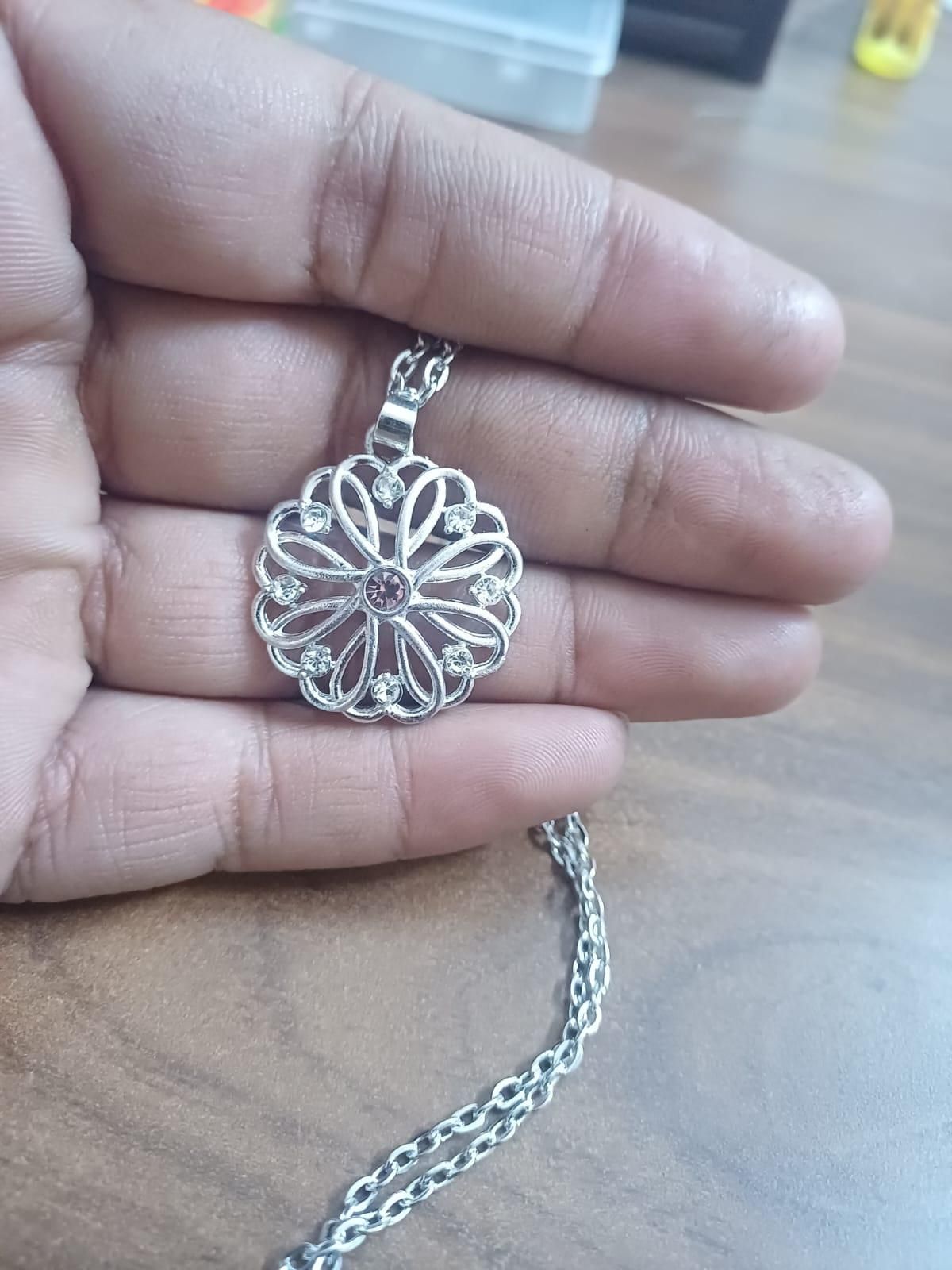 A silver birthstone pendant with a floral design, featuring a purple stone in the center, attached to a silver chain.