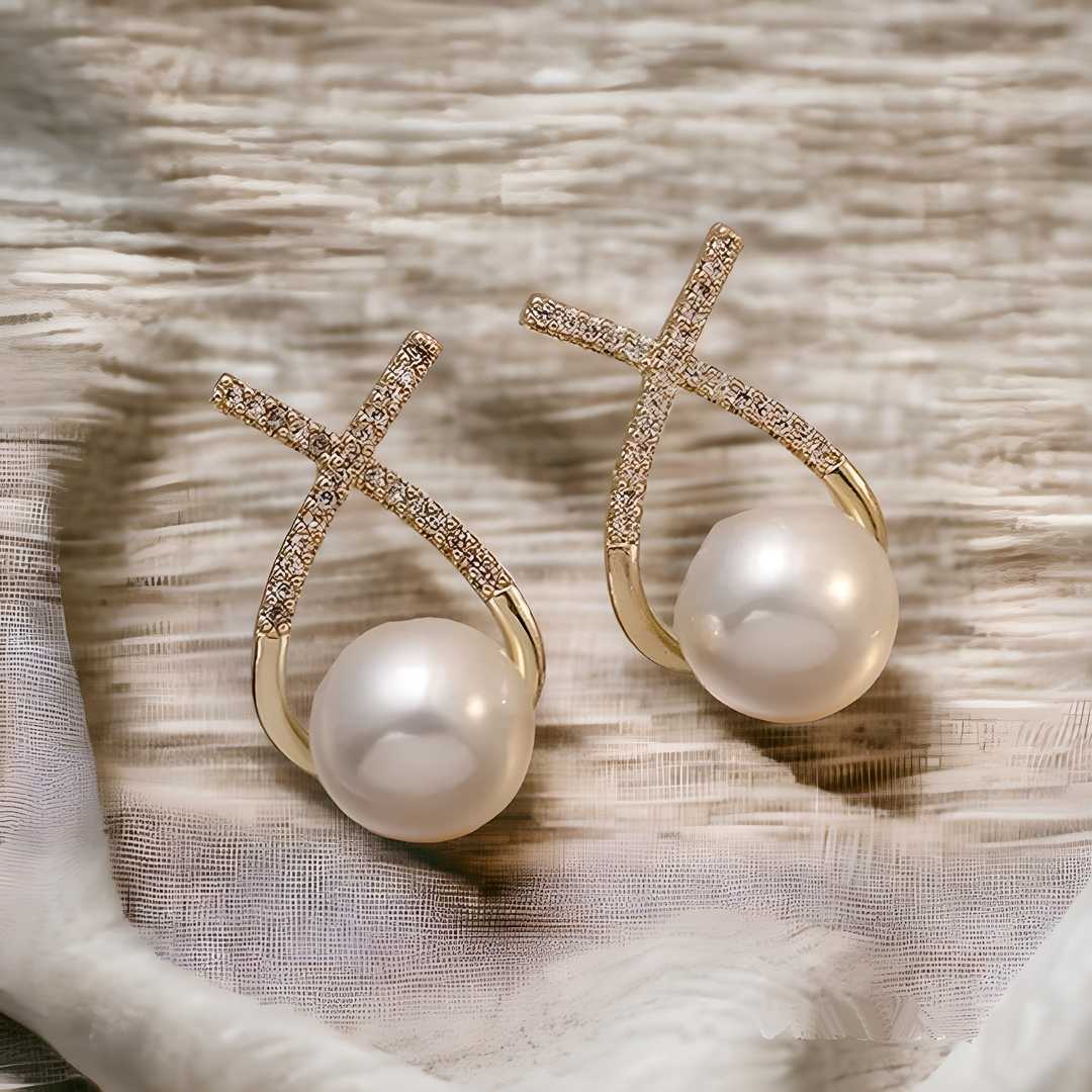 A pair of gold and silver platted cross pearl stud earrings with multicolor stones, displayed on a fabric surface.