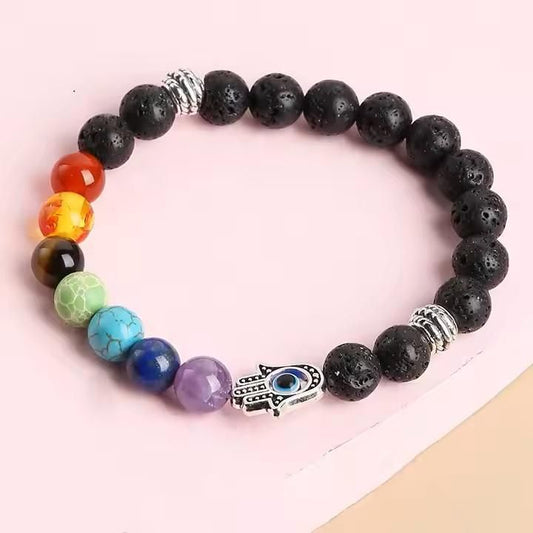 A multicolored beaded bracelet with a black lava stone base and a silver-colored hamsa hand charm, displayed against a light background.