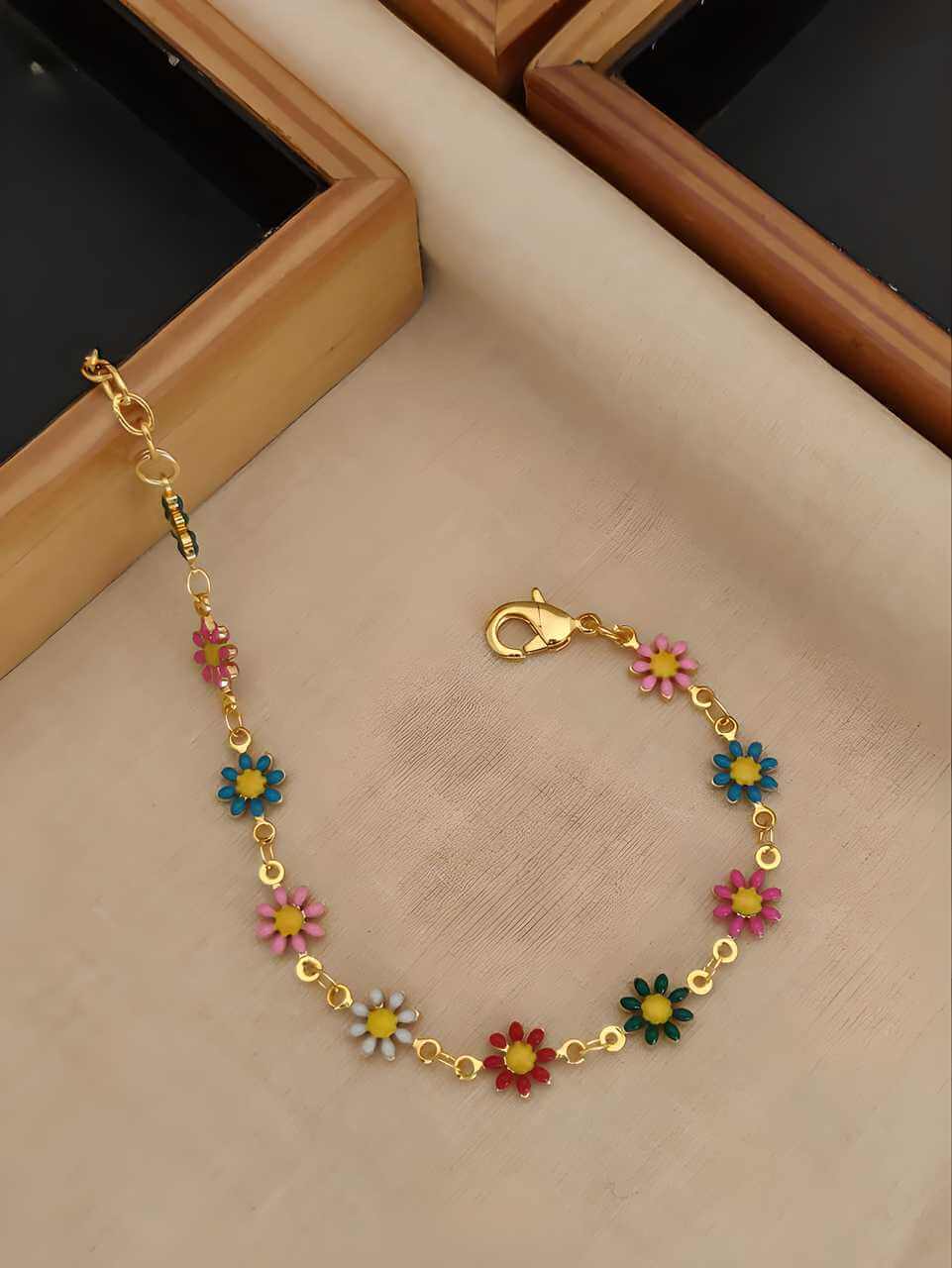 Gold bracelet with colorful flower charms on a beige surface