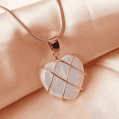 Heart-shaped pendant with rose gold wire wrapping on a soft pink fabric background