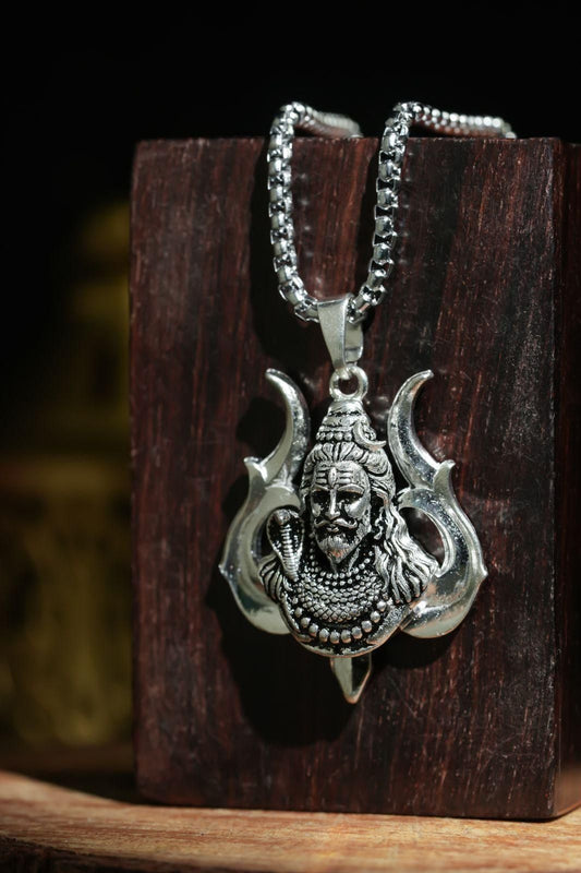 A silver-colored stainless steel chain necklace with a Hanuman pendant, displayed against a wooden backdrop.