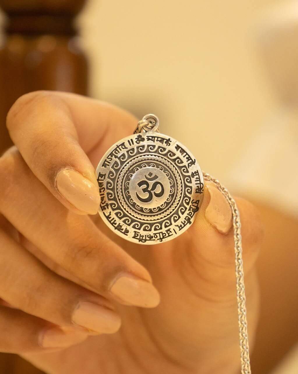 Hand holding a silver pendant with an Om symbol against a blurred background