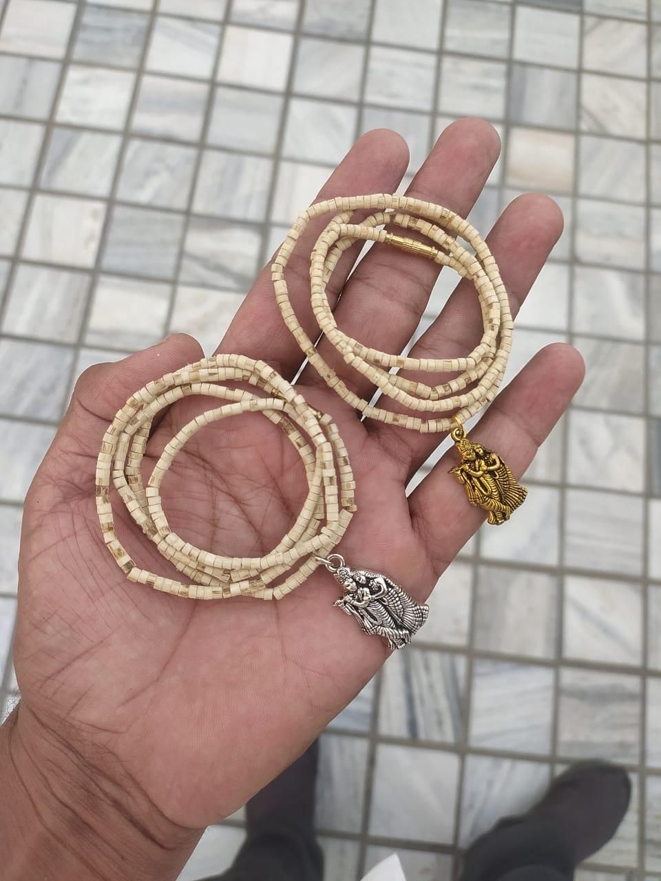 Two wooden Tulsi Mala necklaces with pendants, one depicting a bird and the other a geometric pattern, displayed against a wooden background.