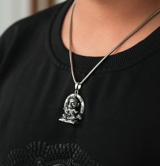 A person wearing a black shirt with a silver-colored Lord Bal Hanuman pendant on a chain around their neck.