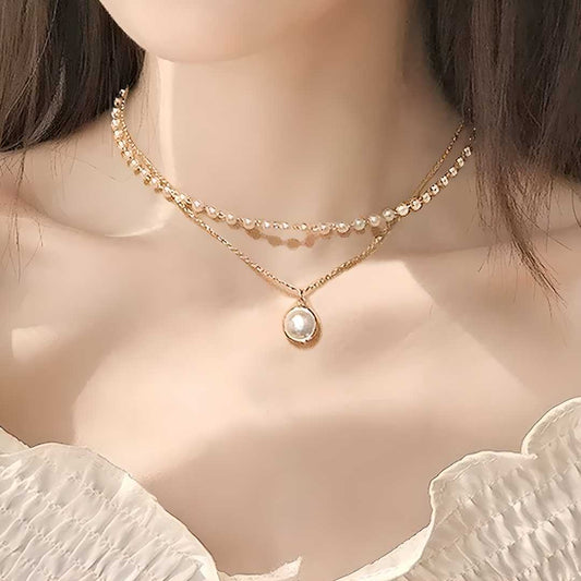 A woman wearing a gold-plated chain necklace with a pearl pendant, layered with a shorter, beaded chain necklace.