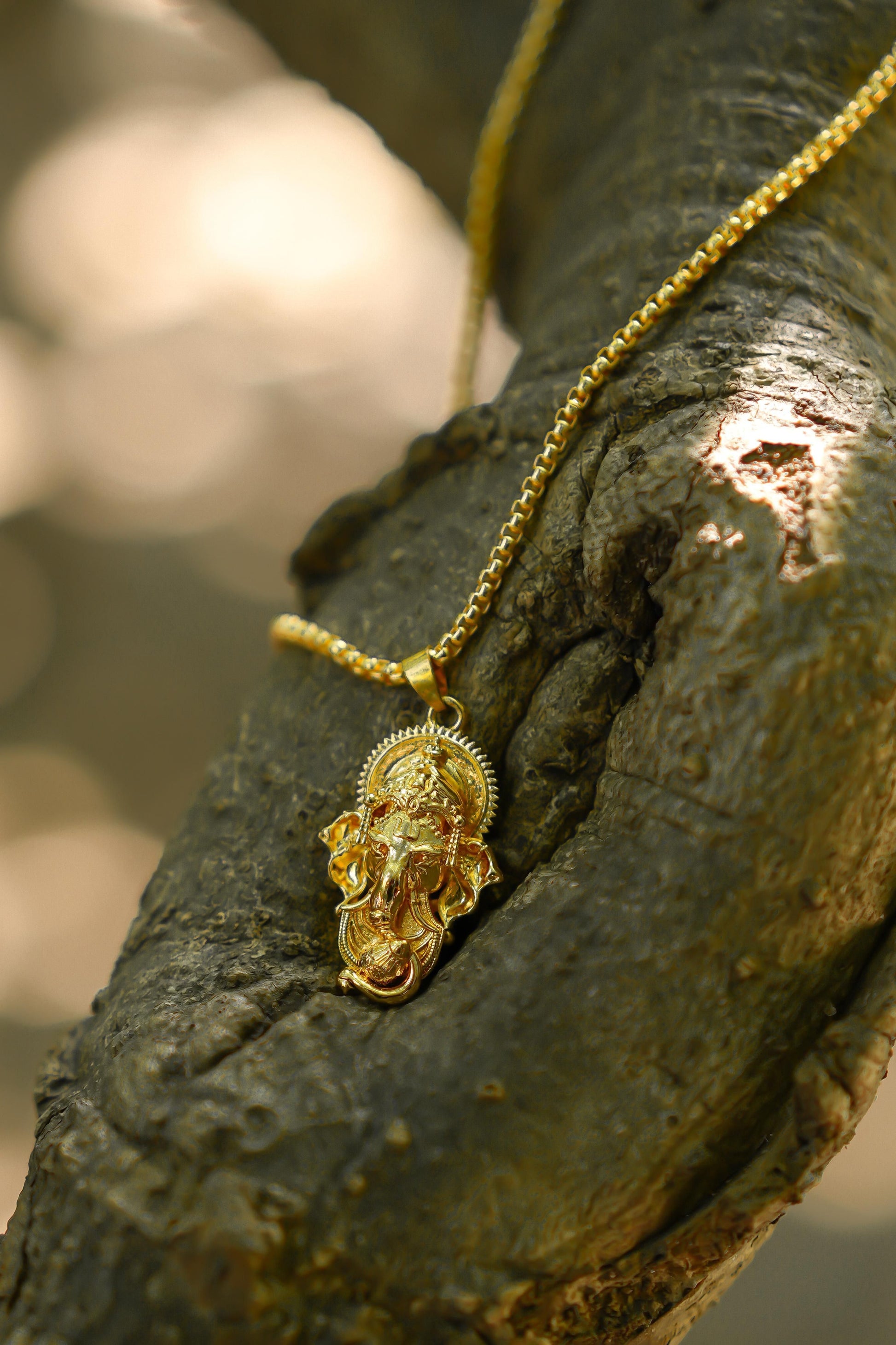 A gold-colored Ganesha pendant attached to a snake chain