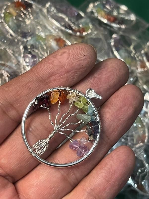 A silver-colored Tree of Life pendant with multicolored chakra stones arranged in a circle,