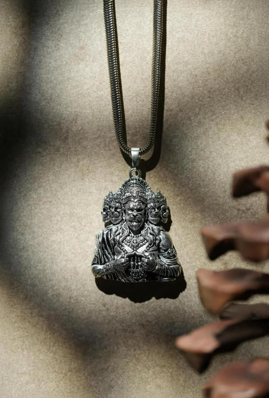 A silver-colored Panchamukhi Hanuman pendant attached to a snake chain, displayed against a natural outdoor background.