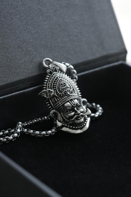 A silver stainless steel pendant in the shape of a Lord Shyam maharaj figure, displayed with a chain on a black surface.