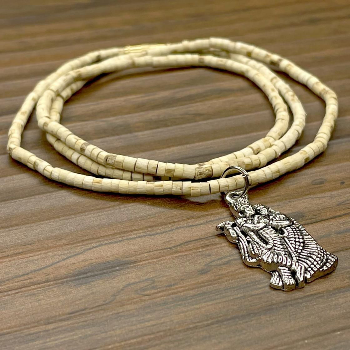 Two wooden Tulsi Mala necklaces with pendants, one depicting a bird and the other a geometric pattern, displayed against a wooden background.