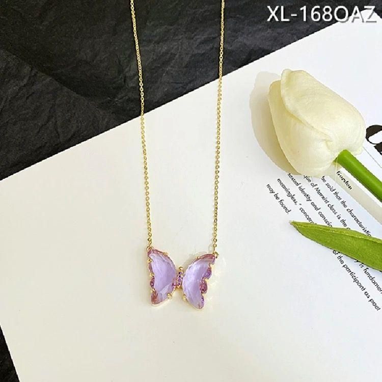 A gold-plated necklace with a stylish butterfly pendant, featuring multicolor (purple and pink) accents on a chain, displayed against a pink fabric background.