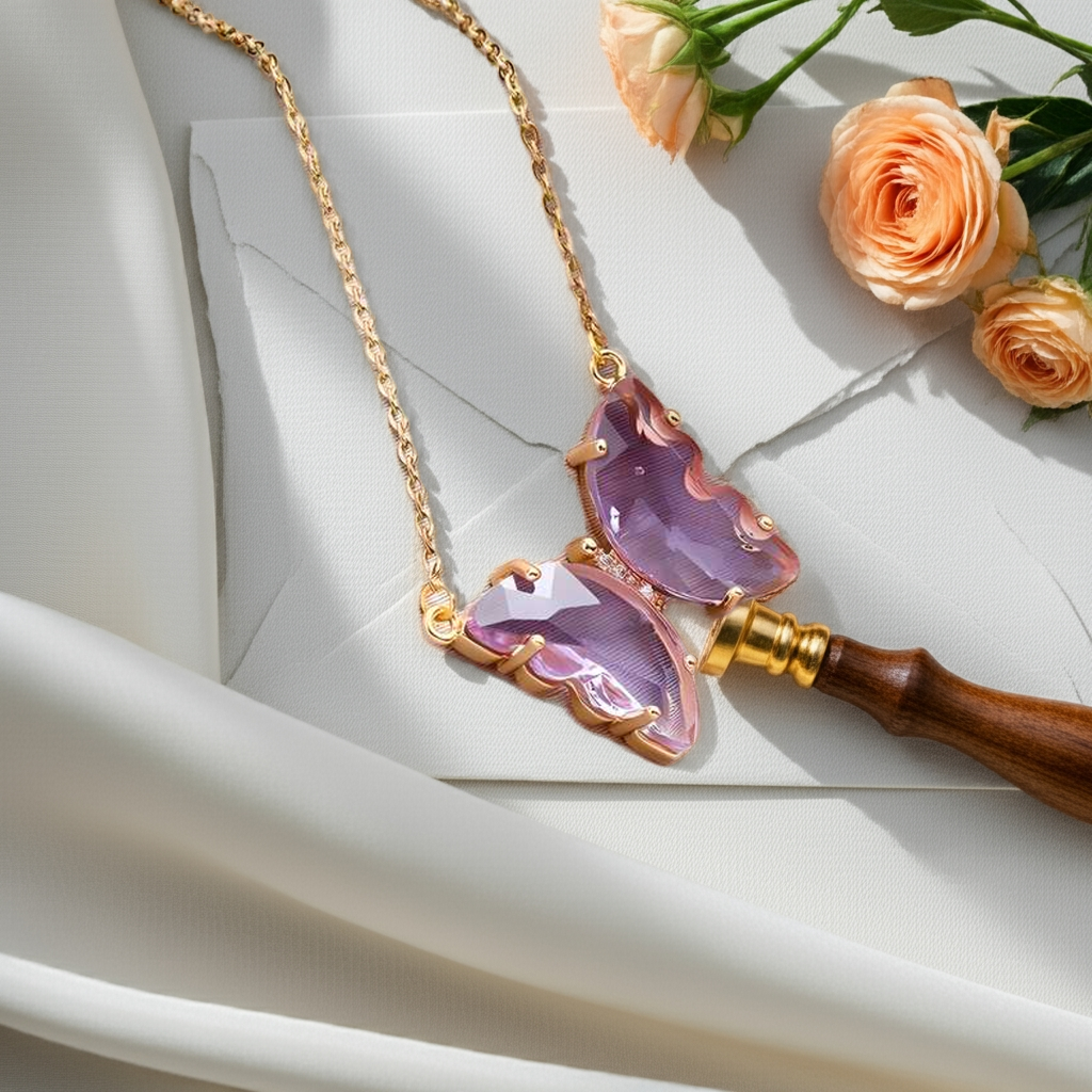 A gold-plated necklace with a stylish butterfly pendant, featuring multicolor (purple and pink) accents on a chain, displayed against a pink fabric background.
