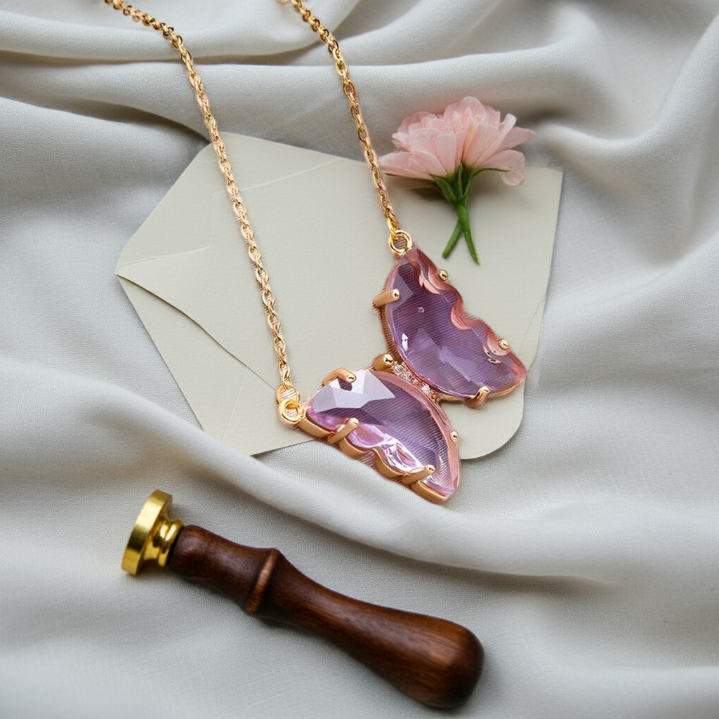 A gold-plated necklace with a stylish butterfly pendant, featuring multicolor (purple and pink) accents on a chain, displayed against a pink fabric background.